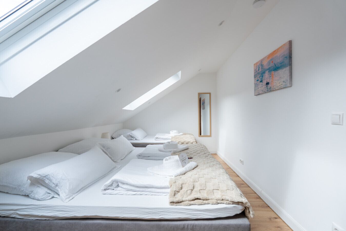 Una camera da letto moderna e luminosa con lucernari, un letto con lenzuola bianche, un comodino e un quadro appeso alla parete.