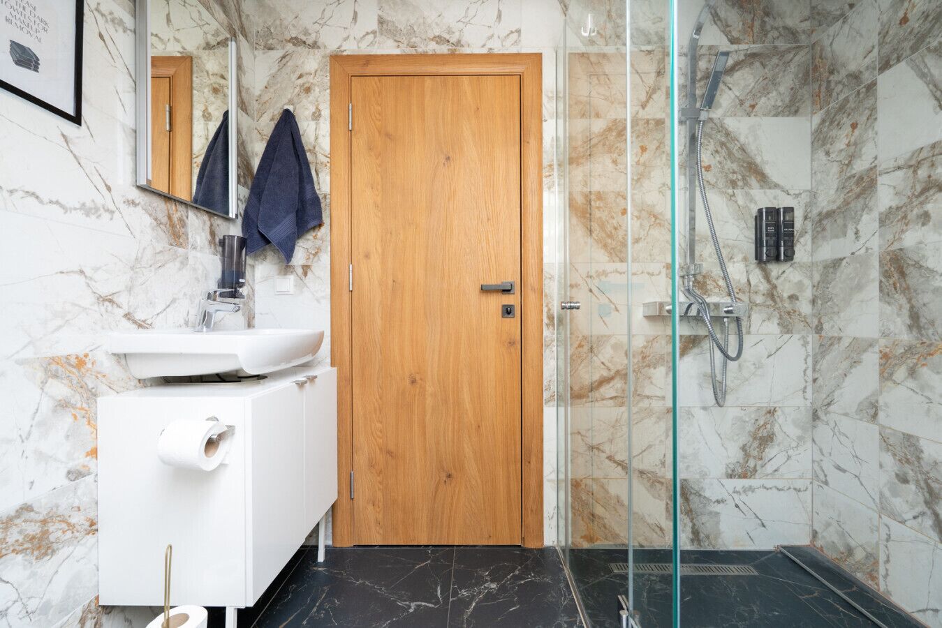 A bathroom with a wooden door, a white sink, a mirror, and a glass-enclosed shower area.