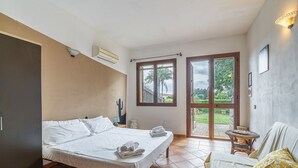 A bedroom with a bed, a sofa, a small table, and a sliding glass door leading to a garden. - Apartment 'Pathos Retreat Mandorlo' with Shared Pool, Wi-Fi and Air Conditioning (Arenella)