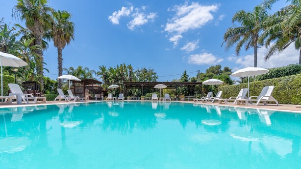 A clear blue pool with lounge chairs and umbrellas, surrounded by palm trees and a clear sky. - Apartment 'Pathos Retreat Ulivo' with Shared Pool, Wi-Fi and Air Conditioning (Arenella)
