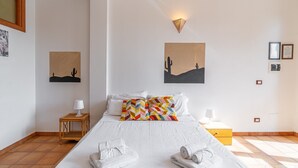 A hotel room with a bed, two wall-mounted paintings, a nightstand, a lamp, and a yellow dresser. - Apartment 'Pathos Retreat Ulivo' with Shared Pool, Wi-Fi and Air Conditioning (Arenella)