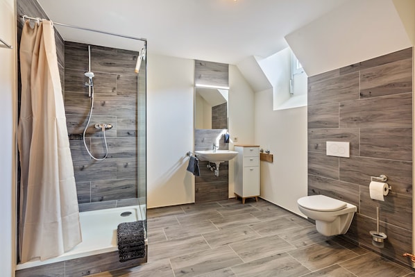 Ein modernes Badezimmer mit Dusche, Waschbecken, Toilette und Spiegel.