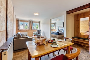A cozy room with a wooden floor, a dining table with plates and a basket of bread, a sofa, and a window with curtains. - Holiday Apartment '5' with Mountain View and Wi-Fi (Sankt Blasien)