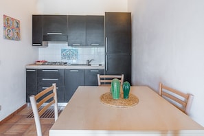 A modern kitchen with dark cabinets, a tiled backsplash, and a wooden dining table with chairs. - Apartment 'Pathos Retreat Carrubbo' with Shared Pool, Wi-Fi and Air Conditioning (Arenella)