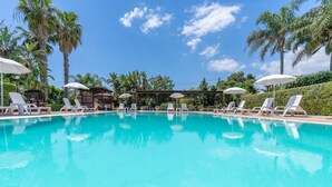 Una piscina azul cristalina con sillas de descanso y sombrillas, rodeada de palmeras y un cielo despejado.