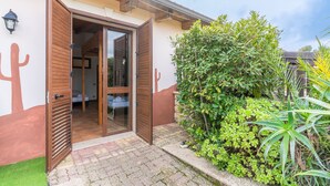 A hotel entrance with a wooden door, a glass door leading inside, and a small garden area with green plants and a cactus decoration on the wall. - Apartment 'Pathos Retreat Limone' with Shared Pool, Wi-Fi and Air Conditioning (Arenella)