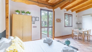 A bedroom with a bed, a wooden wardrobe, a dining area with a table and chairs, and a view through a glass door. - Apartment 'Pathos Retreat Limone' with Shared Pool, Wi-Fi and Air Conditioning (Arenella)