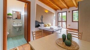 A room with a bed, a table with decorative items, a bathroom with a sink and mirror, and a wooden ceiling. - Apartment 'Pathos Retreat Zagara' with Shared Pool, Wi-Fi and Air Conditioning (Arenella)