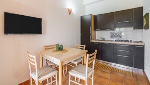 A modern kitchen with dark cabinets, a flat-screen TV, and a dining table with chairs. - Apartment 'Pathos Retreat Zagara' with Shared Pool, Wi-Fi and Air Conditioning (Arenella)