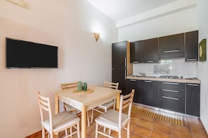 Une cuisine moderne avec des meubles de rangement aux couleurs foncées, un téléviseur à écran plat et une table à manger avec des chaises.