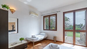 Quarto com cama, mesa de cabeceira com planta, janela e ar-condicionado.