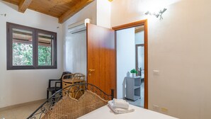 A bedroom with a bed, a wooden door, a window, a chair, and a small table. - Apartment 'Pathos Retreat Rosmarino' with Shared Pool, Wi-Fi and Air Conditioning (Arenella)