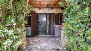 A stone-paved entrance with a wooden ceiling, a door leading to a room, and surrounding greenery. - Apartment 'Pathos Retreat Rosmarino' with Shared Pool, Wi-Fi and Air Conditioning (Arenella)