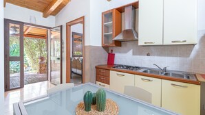 A modern kitchen with a glass-top table, wooden cabinets, and a view through the open door. - Apartment 'Pathos Retreat Rosmarino' with Shared Pool, Wi-Fi and Air Conditioning (Arenella)