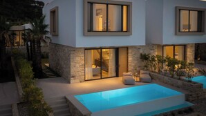 Una moderna casa a due piani con piscina, muri in pietra e ampie finestre.