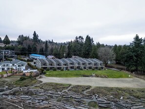 A row of modern, multi-story buildings with a flat roof design, surrounded by dense forest. - #201 Lower Garden View Suite at Shorewater Resort, Qualicum Beach (Qualicum Beach)