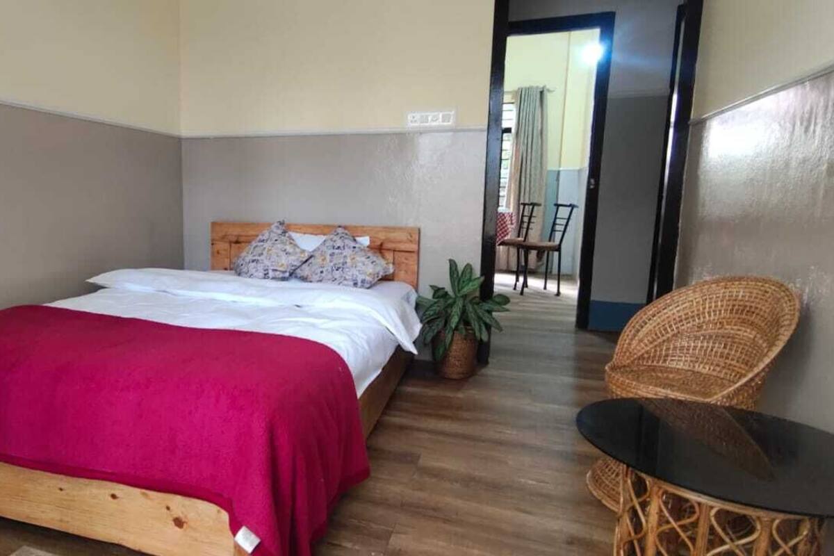 A bedroom with a wooden bed, a red bedspread, a small table, and a wicker chair.