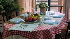 A dining table set with a red and white checkered tablecloth, a fruit bowl, plates, cutlery, and a potted plant. - Beltola Lodge - a serene homestay (Guwahati)