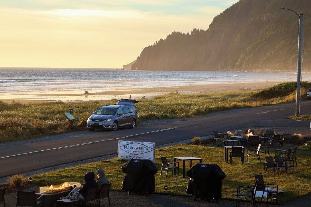 A restaurant with outdoor seating overlooking a beach, a parked car, and a sign indicating the restaurant is now open.