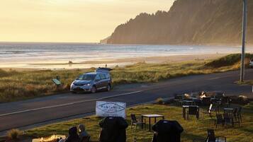 A restaurant with outdoor seating overlooking a beach, a parked car, and a sign indicating the restaurant is now open.