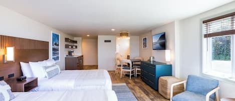Habitación de hotel con dos camas, un escritorio, una silla, un televisor y una ventana con persianas.