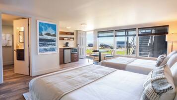 Habitación de hotel con dos camas, zona de comedor, cocina y vista al océano.