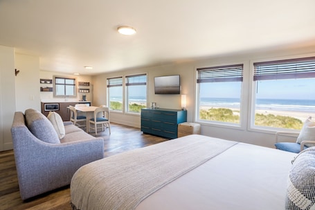 A bedroom with a large bed, a sofa, a dresser, a TV, and a view of the beach.