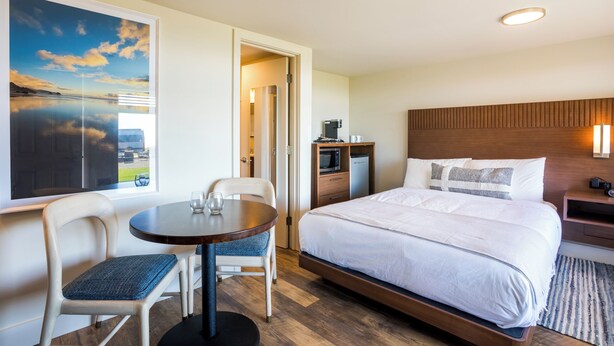 A hotel room with a bed, a dining table with chairs, a microwave, a coffee maker, and a large window with a view. - Manzanita Oceanfront Inn (Manzanita)