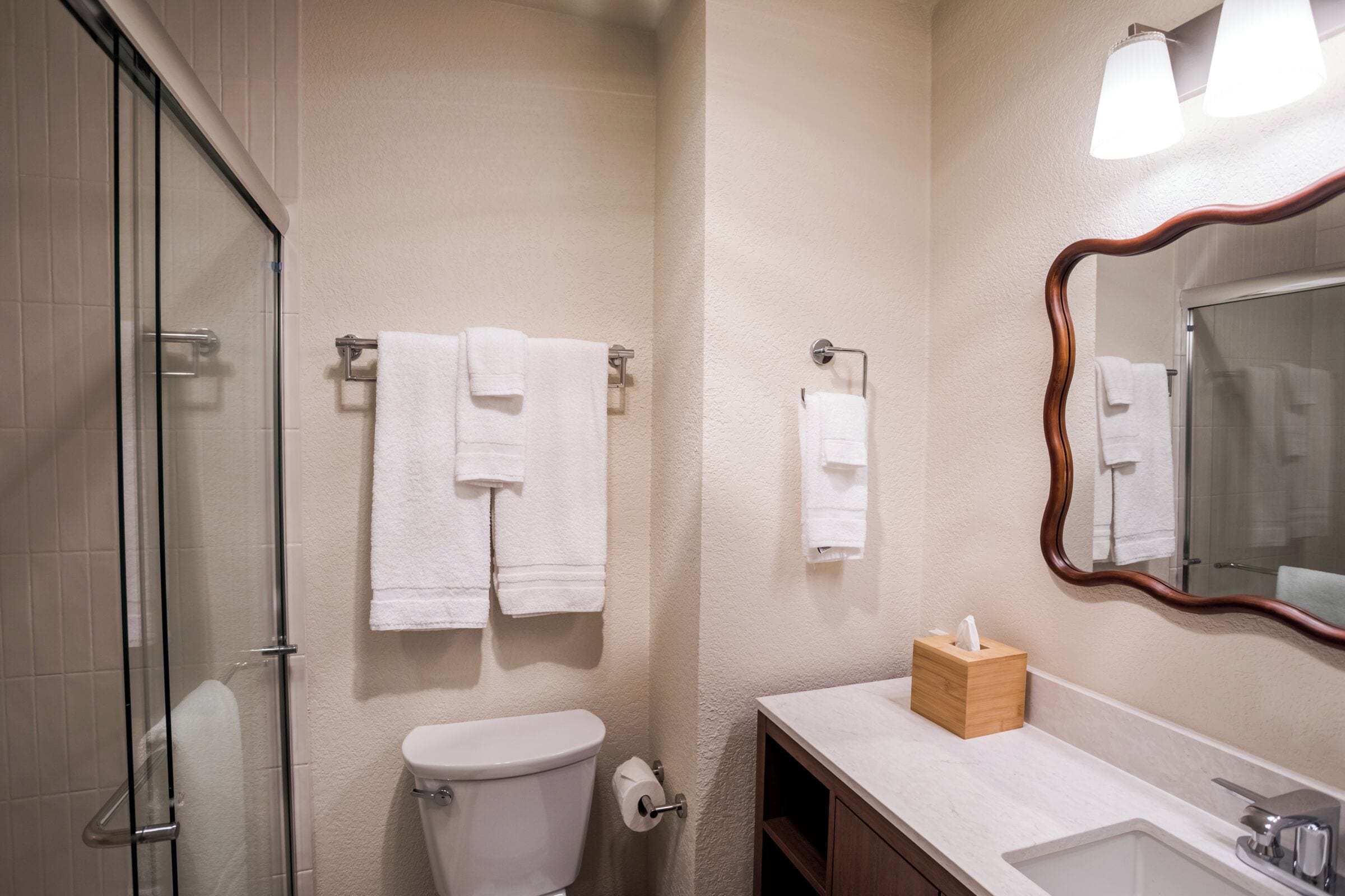 A bathroom with a glass shower enclosure, a toilet, a sink with a mirror, and towels on towel racks.