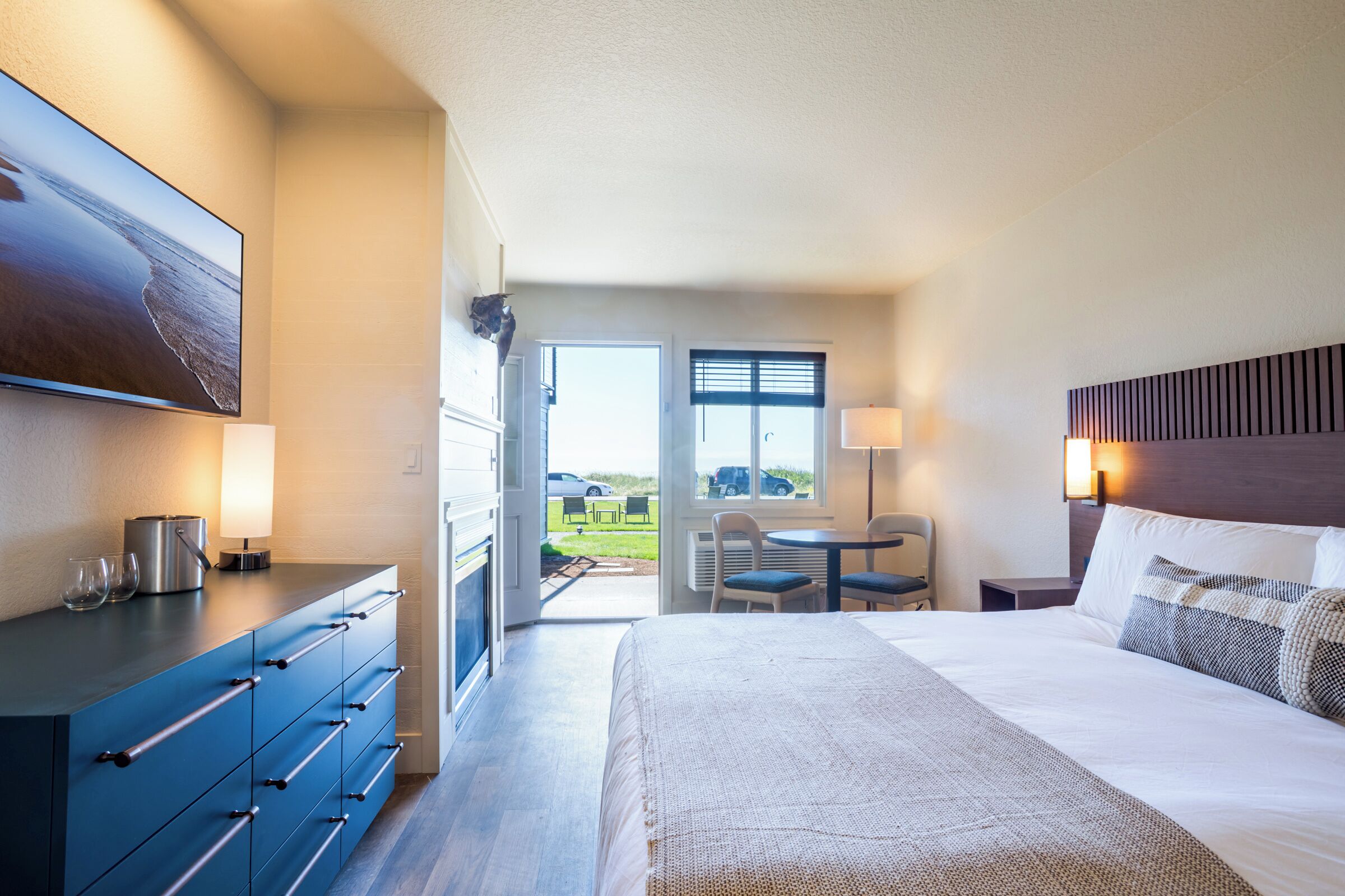 Ein Hotelzimmer mit Bett, Schreibtisch mit Lampe, Stuhl, Esstisch mit Stühlen und Blick ins Freie.