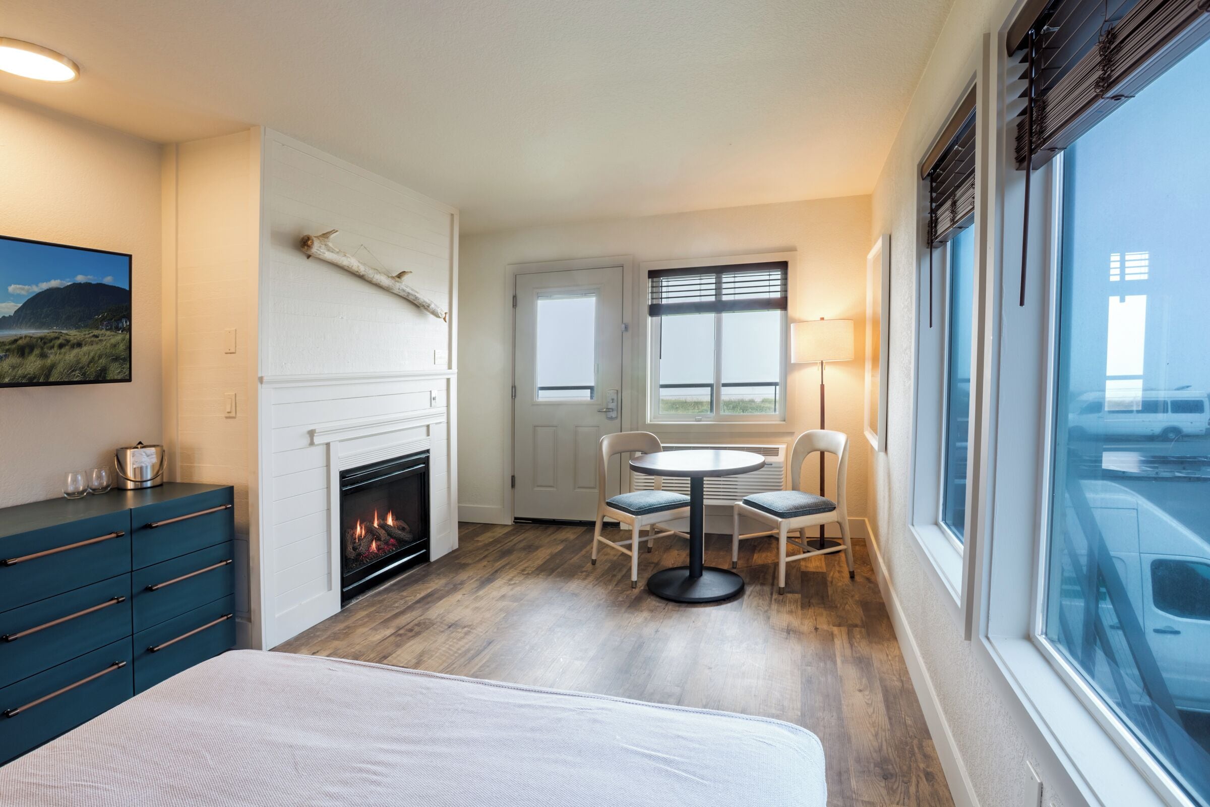 A room with a fireplace, a dining table with chairs, a bed, and a large window with a view.
