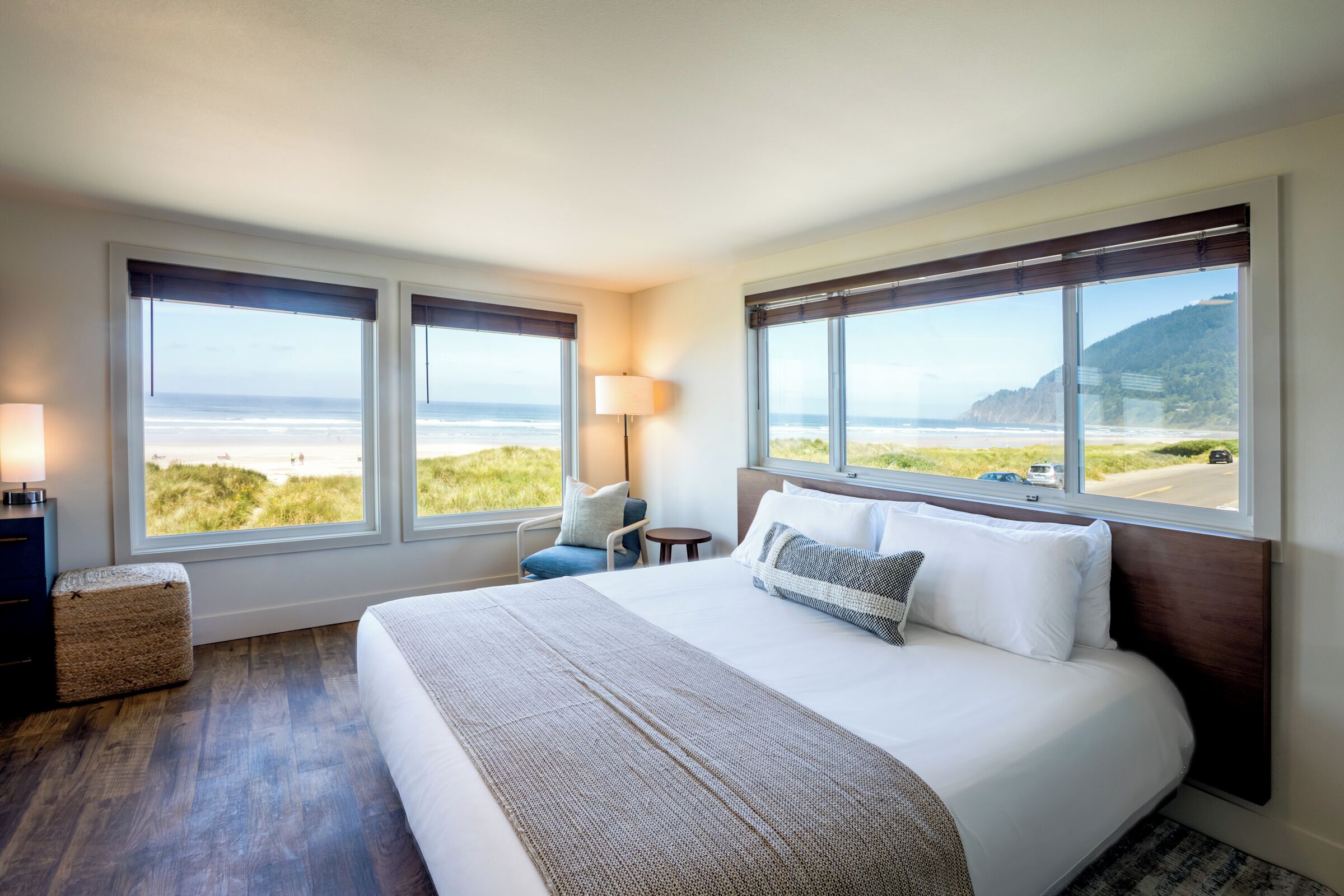 Une chambre d’hôtel avec un grand lit, deux fenêtres donnant sur la plage, une lampe de chevet et une petite table.