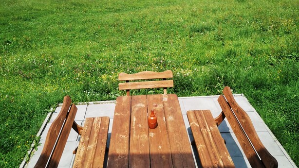 Une table de pique-nique avec des bancs, installée dans un champ herbeux, avec une vue sur des collines en arrière-plan.