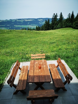Una mesa de picnic con bancos en un campo cubierto de hierba, con vistas a colinas al fondo.