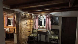 Une pièce rustique avec des murs en bois, un banc en bois, deux chaises, une table et une porte.