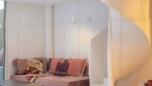 A modern interior with a curved white wall, a sofa with patterned cushions, and a small table. - Private Patio / Gym / Sauna / Loft / Fast Wifi (Dubai)