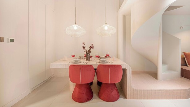 A dining area with a white table, red chairs, and hanging pendant lights. - Private Patio / Gym / Sauna / Loft / Fast Wifi (Dubai)