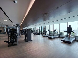 Ein modernes Fitnessstudio mit Laufbändern, Krafttrainingsgeräten und großen Fenstern mit Blick auf die Stadt.