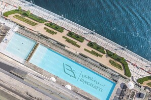 Ein Luftbild eines Anwesens am Wasser mit einem großen Pool, einer Promenade und Blick auf das Meer.