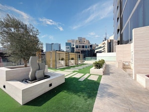 A rooftop garden with artificial grass, a modern water feature, and a seating area. - Chic Studio w/ Private Jacuzzi / Cold Plunge / Gym (Dubai)