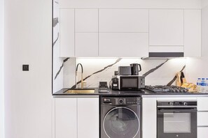 A modern kitchen with a built-in washer and dryer, a microwave, a coffee maker, and a gas stove. - Chic Studio w/ Private Jacuzzi / Cold Plunge / Gym (Dubai)