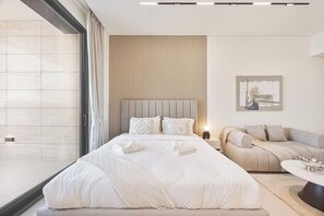 A modern hotel room with a large bed, a sofa, and a dining table. - Chic Studio w/ Private Jacuzzi / Cold Plunge / Gym (Dubai)