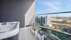 Un balcone moderno con vasca idromassaggio, una sedia e un tavolo con vista su un porto turistico e palazzi alti.
