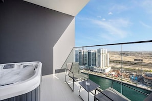 A modern balcony with a hot tub, a chair, and a table overlooking a marina and high-rise buildings. - Chic Studio w/ Private Jacuzzi / Cold Plunge / Gym (Dubai)