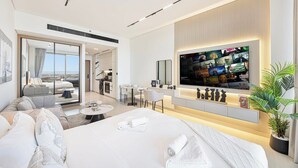Una moderna camera d'albergo con un letto grande, una TV a parete, un angolo salotto con divano e poltrone, e vista panoramica attraverso la porta vetrata.
