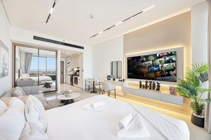 A modern hotel room with a large bed, a TV mounted on the wall, a seating area with a sofa and chairs, and a view through the glass door. - Chic Studio w/ Private Jacuzzi / Cold Plunge / Gym (Dubai)