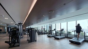 Una palestra moderna con attrezzature cardio, macchinari per pesi e ampie finestre con vista sulla città.