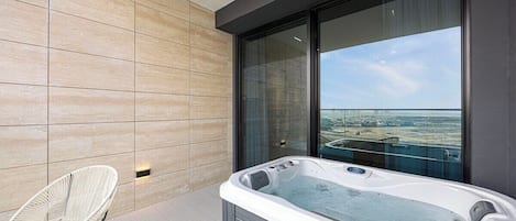 Un balcon moderne avec un jacuzzi, deux fauteuils en osier et une vue sur la ville.