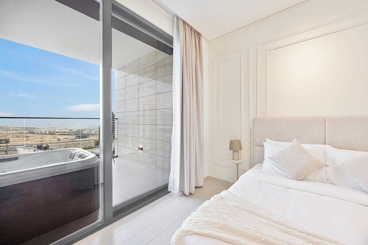 Een hotelkamer met een grote schuifpui die uitkomt op een balkon, een bed met witte lakens en een nachtkastje met een lamp.