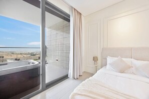 Habitació d'hotel amb una gran porta corredissa de vidre que dona a un balcó, un llit amb roba blanca i una tauleta de nit amb una làmpada.